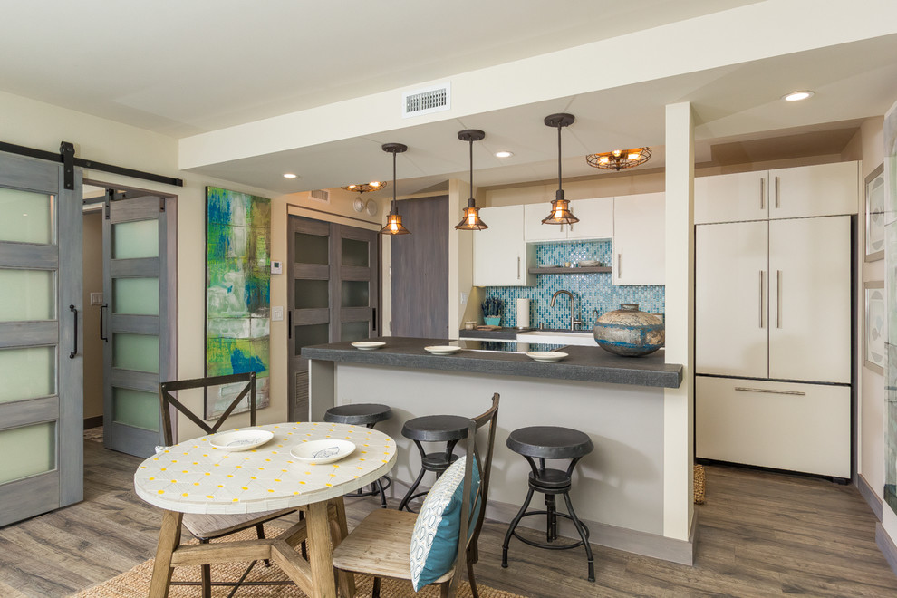 Zweizeilige Maritime Wohnküche mit dunklem Holzboden, flächenbündigen Schrankfronten, weißen Schränken, Küchenrückwand in Blau, Elektrogeräten mit Frontblende und Kücheninsel in San Diego