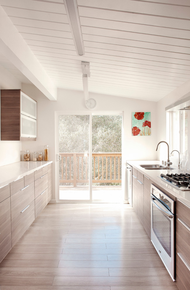 Exemple d'une cuisine parallèle moderne en bois clair de taille moyenne avec un évier 2 bacs, un placard à porte plane, un électroménager en acier inoxydable, parquet clair et un sol marron.
