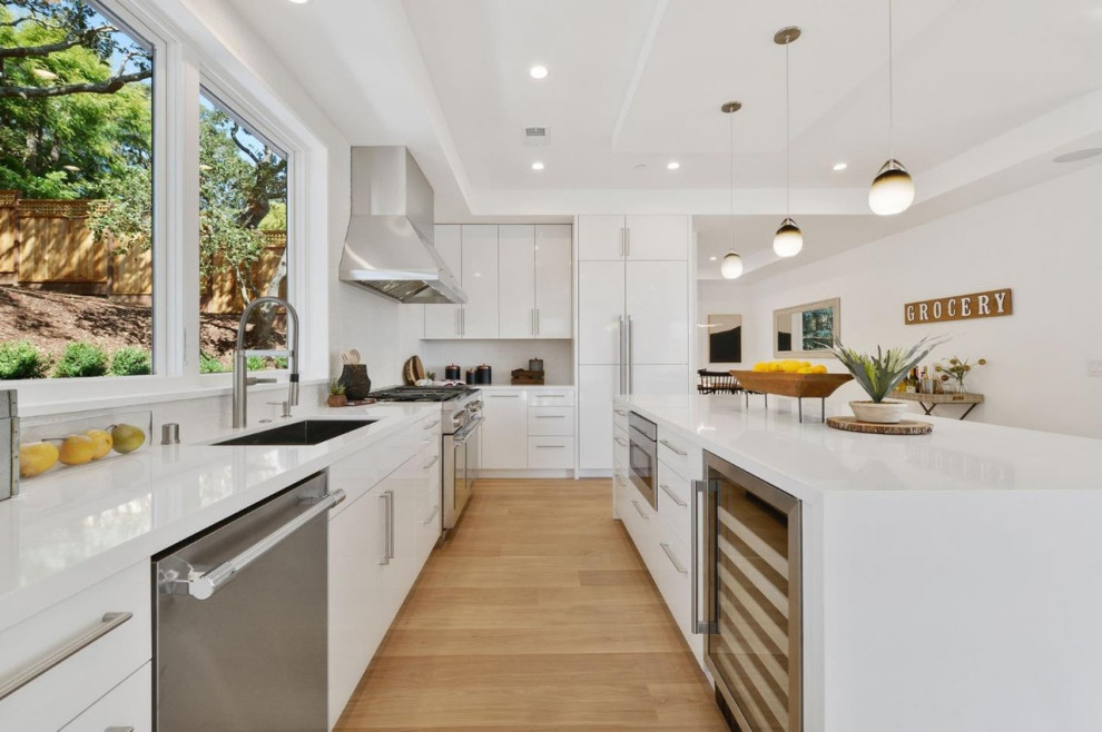 Example of a mid-sized minimalist l-shaped medium tone wood floor and yellow floor eat-in kitchen design in San Francisco with an undermount sink, flat-panel cabinets, white cabinets, quartz countertops, white backsplash, porcelain backsplash, stainless steel appliances, an island and white countertops