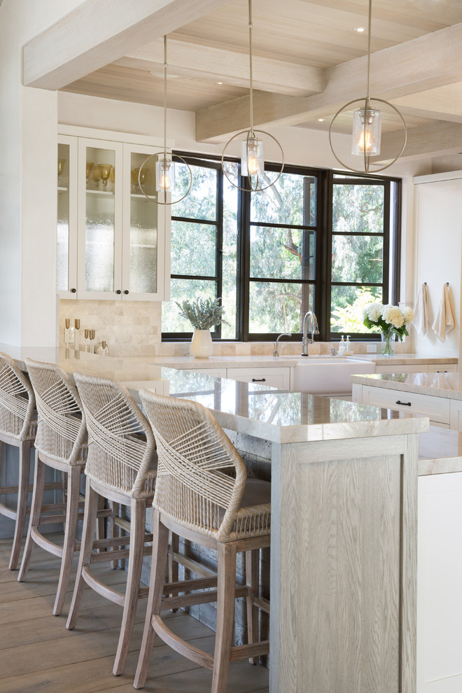 Example of a large tuscan l-shaped light wood floor and beige floor open concept kitchen design in Santa Barbara with an undermount sink, shaker cabinets, white cabinets, quartzite countertops, beige backsplash, stone tile backsplash, stainless steel appliances, an island and beige countertops