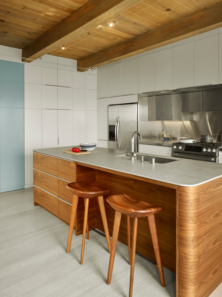 Modern inredning av ett l-kök, med en undermonterad diskho, släta luckor, vita skåp, stänkskydd med metallisk yta, stänkskydd i metallkakel, rostfria vitvaror och en köksö