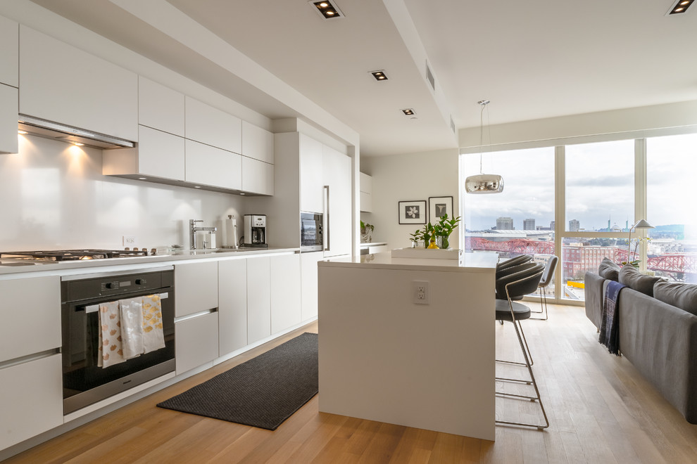 Offene, Einzeilige Moderne Küche mit flächenbündigen Schrankfronten, weißen Schränken, Küchenrückwand in Weiß, Küchengeräten aus Edelstahl, hellem Holzboden und Kücheninsel in Portland