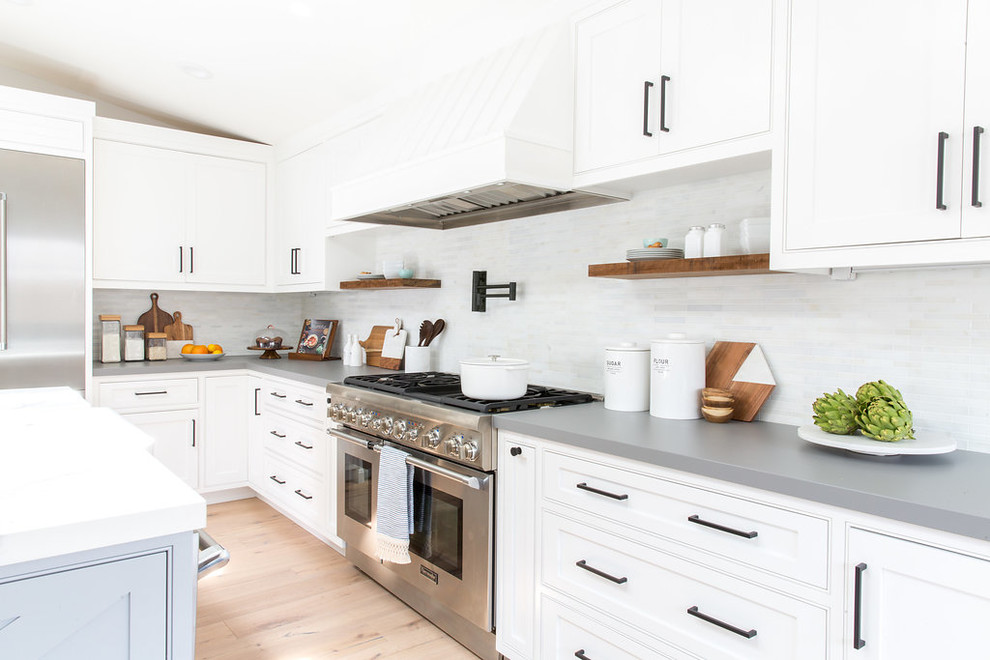 This is an example of a large rural open plan kitchen in Los Angeles with white cabinets, marble worktops, grey splashback, black appliances, light hardwood flooring and an island.