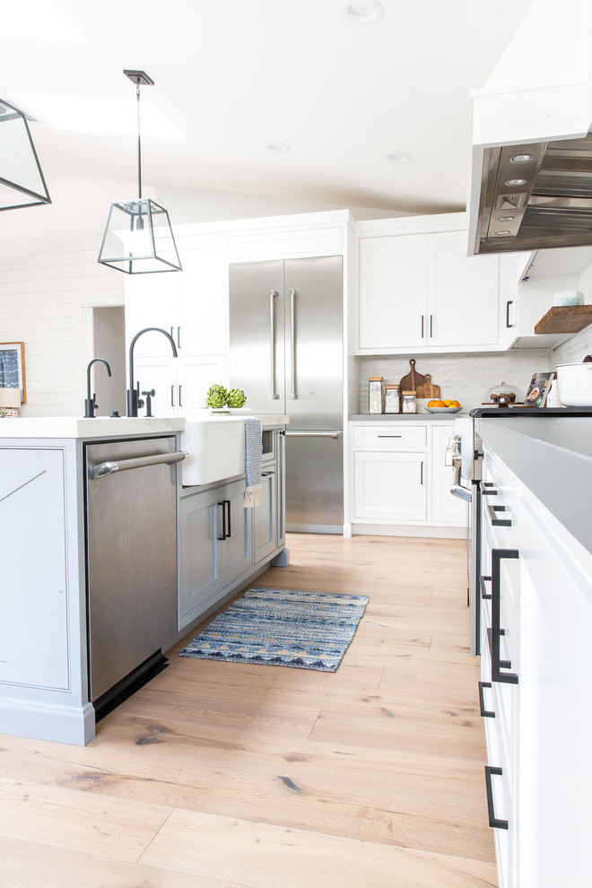 Immagine di una grande cucina country con ante bianche, top in marmo, paraspruzzi grigio, elettrodomestici neri e parquet chiaro