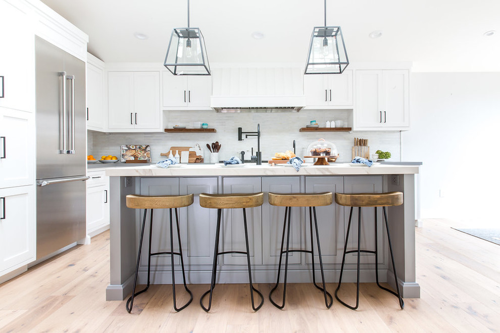 Inspiration for a large country open plan kitchen in Los Angeles with white cabinets, marble worktops, grey splashback, black appliances, light hardwood flooring and an island.