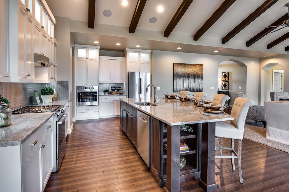 Klassisk inredning av ett stort kök, med en dubbel diskho, luckor med infälld panel, vita skåp, granitbänkskiva, grått stänkskydd, rostfria vitvaror, vinylgolv, en köksö och brunt golv