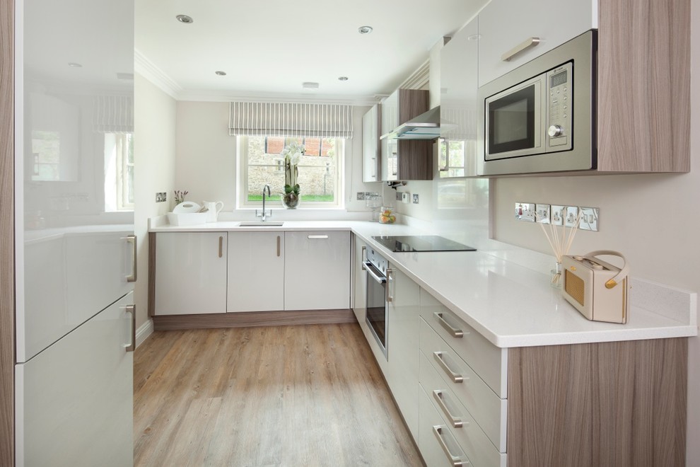 Kleine Moderne Wohnküche ohne Insel mit integriertem Waschbecken, weißen Schränken, Granit-Arbeitsplatte, Elektrogeräten mit Frontblende und hellem Holzboden in Berkshire
