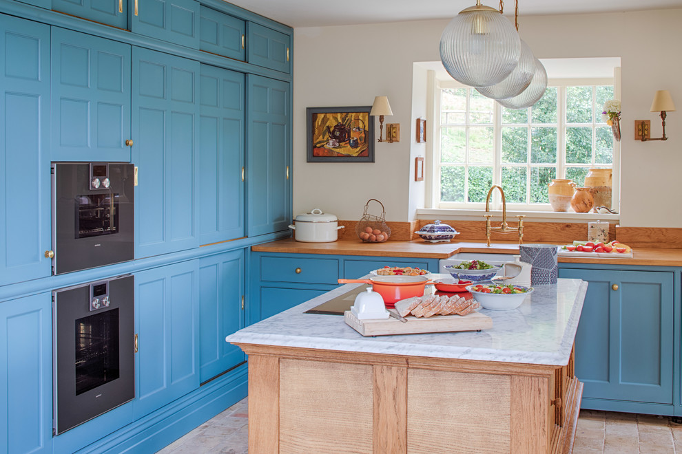 Klassische Küche in L-Form mit Landhausspüle, Kassettenfronten, blauen Schränken, Arbeitsplatte aus Holz, Küchengeräten aus Edelstahl, Kücheninsel, beigem Boden und brauner Arbeitsplatte in Gloucestershire