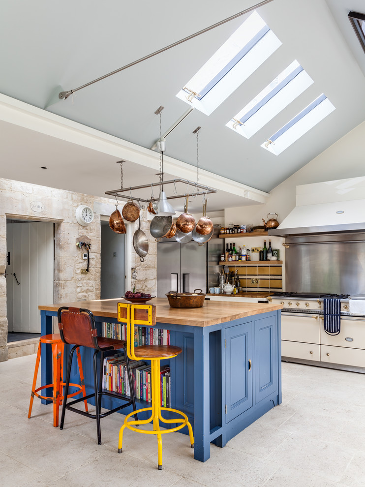 Country white floor kitchen photo in Gloucestershire with blue cabinets, wood countertops, an island, recessed-panel cabinets and white appliances