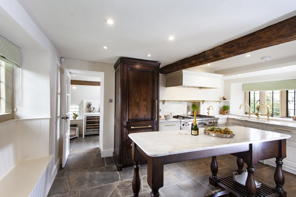 Medium sized traditional l-shaped kitchen in Gloucestershire with a double-bowl sink, marble worktops, white splashback, marble splashback, stainless steel appliances, an island, white worktops, raised-panel cabinets, white cabinets and brown floors.