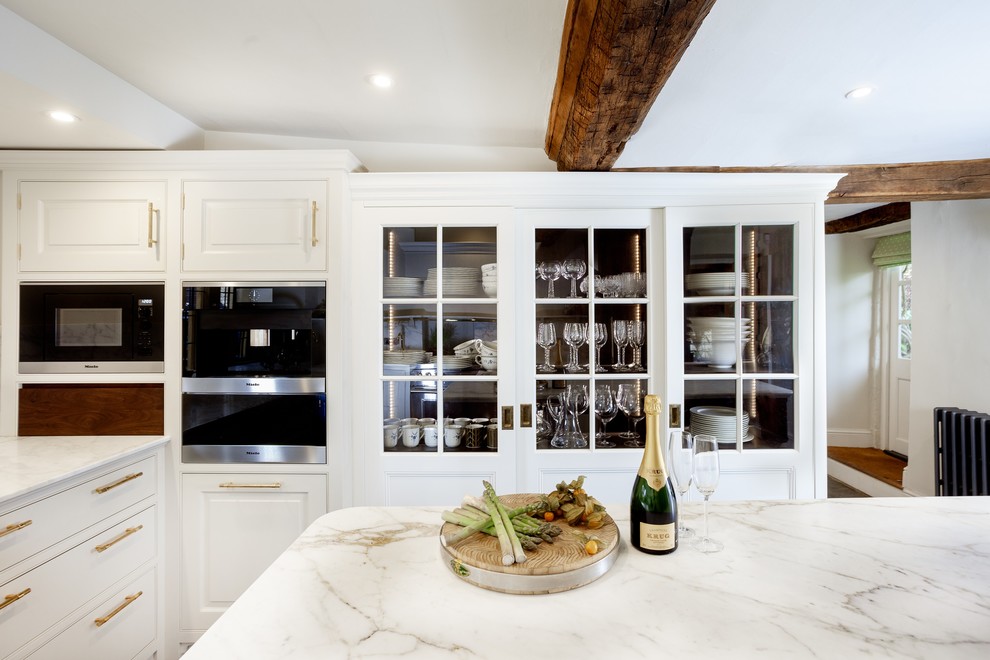 Medium sized traditional u-shaped kitchen/diner in Gloucestershire with a double-bowl sink, recessed-panel cabinets, dark wood cabinets, marble worktops, white splashback, marble splashback, stainless steel appliances, an island, grey floors and white worktops.