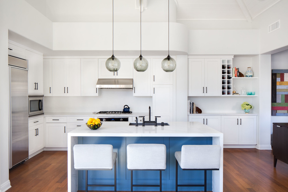 Inspiration for a medium sized contemporary l-shaped open plan kitchen in Orange County with shaker cabinets, white cabinets, engineered stone countertops, white splashback, porcelain splashback, stainless steel appliances, medium hardwood flooring, an island, brown floors, a submerged sink and white worktops.