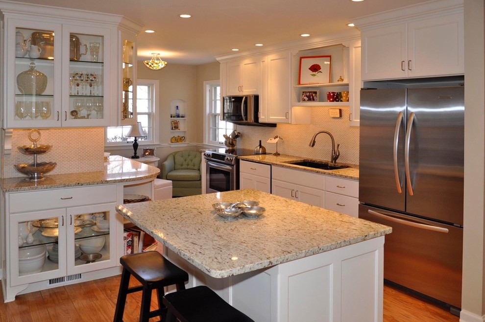 Example of a mid-sized country galley medium tone wood floor enclosed kitchen design in Orange County with a double-bowl sink, shaker cabinets, white cabinets, granite countertops, white backsplash, ceramic backsplash, stainless steel appliances and an island