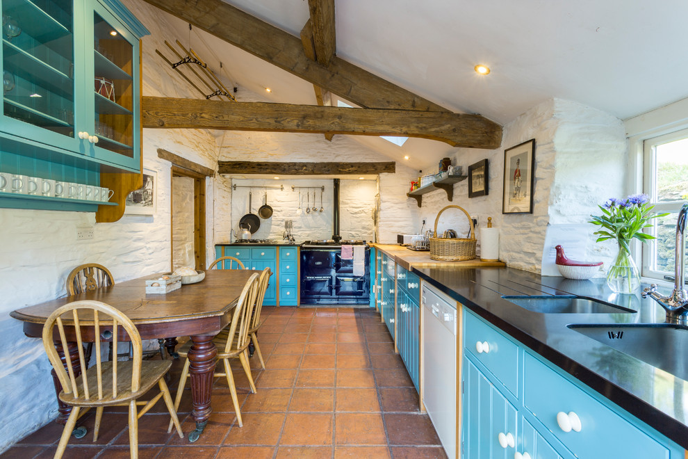 Inspiration for a rural l-shaped kitchen/diner in Cardiff with a double-bowl sink, blue cabinets, black appliances, no island, brown floors and black worktops.