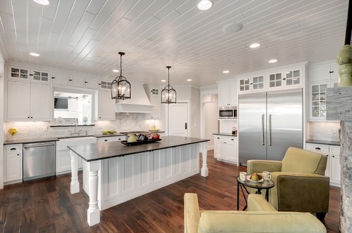 Kitchen & Bathroom Cabinets — white shaker kitchen with dark island, lantern pendants, beadboard ceiling, and stainless pro refrigerator.
