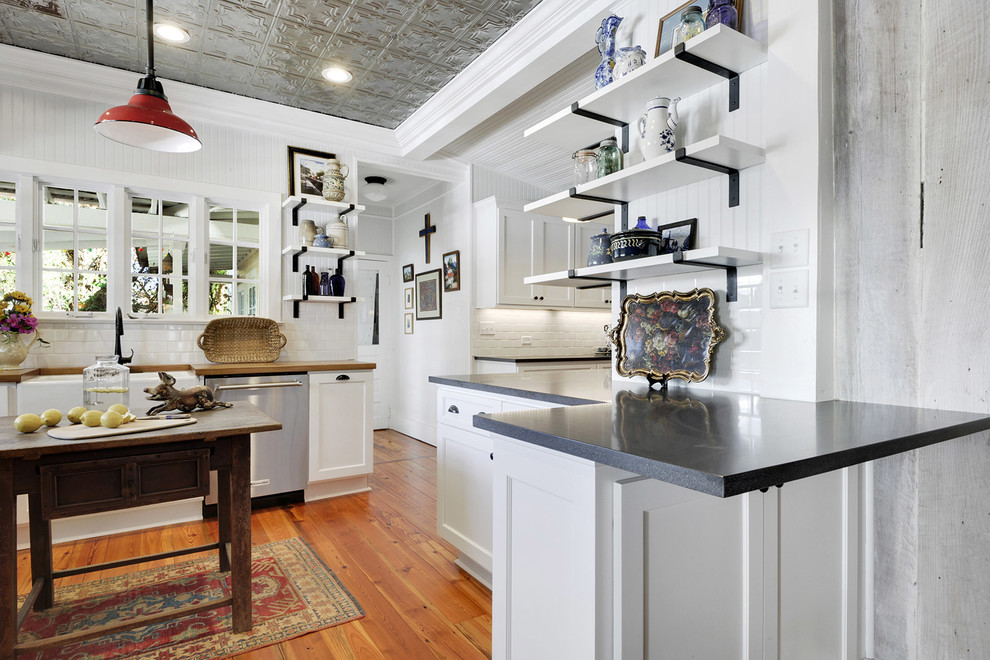 Bild på ett litet lantligt l-kök, med en rustik diskho, skåp i shakerstil, vita skåp, granitbänkskiva, vitt stänkskydd, stänkskydd i tunnelbanekakel, rostfria vitvaror och ljust trägolv