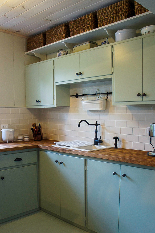 Exempel på ett litet, avskilt lantligt u-kök, med en dubbel diskho, släta luckor, gröna skåp, träbänkskiva, vitt stänkskydd, stänkskydd i tunnelbanekakel, rostfria vitvaror och målat trägolv