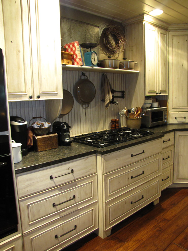Geschlossene, Große Shabby-Look Küche in U-Form mit Landhausspüle, profilierten Schrankfronten, beigen Schränken, Granit-Arbeitsplatte, Küchenrückwand in Beige, schwarzen Elektrogeräten, dunklem Holzboden und Kücheninsel in Sonstige