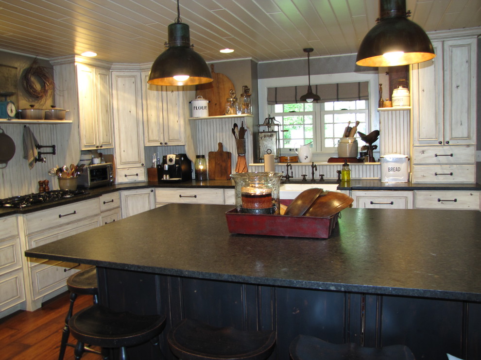 Foto på ett avskilt, stort shabby chic-inspirerat u-kök, med en rustik diskho, luckor med upphöjd panel, beige skåp, granitbänkskiva, beige stänkskydd, svarta vitvaror, mörkt trägolv och en köksö