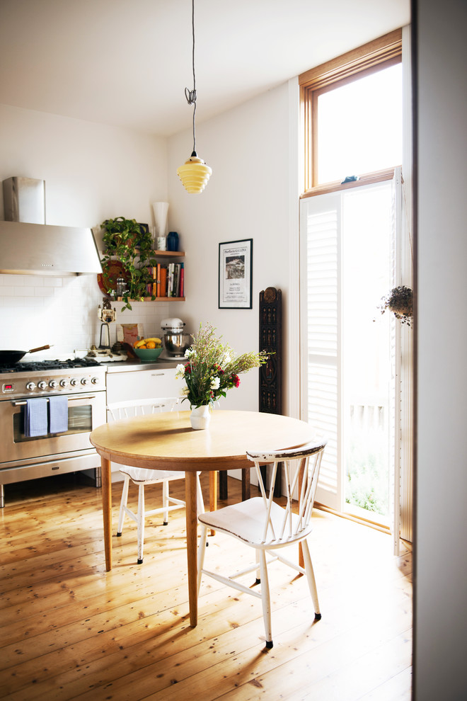 Foto på ett mellanstort nordiskt linjärt kök, med rostfria vitvaror, luckor med profilerade fronter, vita skåp, bänkskiva i rostfritt stål, vitt stänkskydd, stänkskydd i keramik och ljust trägolv
