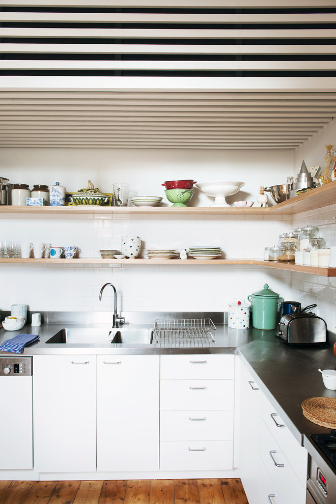Foto på ett mellanstort skandinaviskt l-kök, med en dubbel diskho, luckor med profilerade fronter, vita skåp, bänkskiva i rostfritt stål, vitt stänkskydd, stänkskydd i keramik, rostfria vitvaror och ljust trägolv