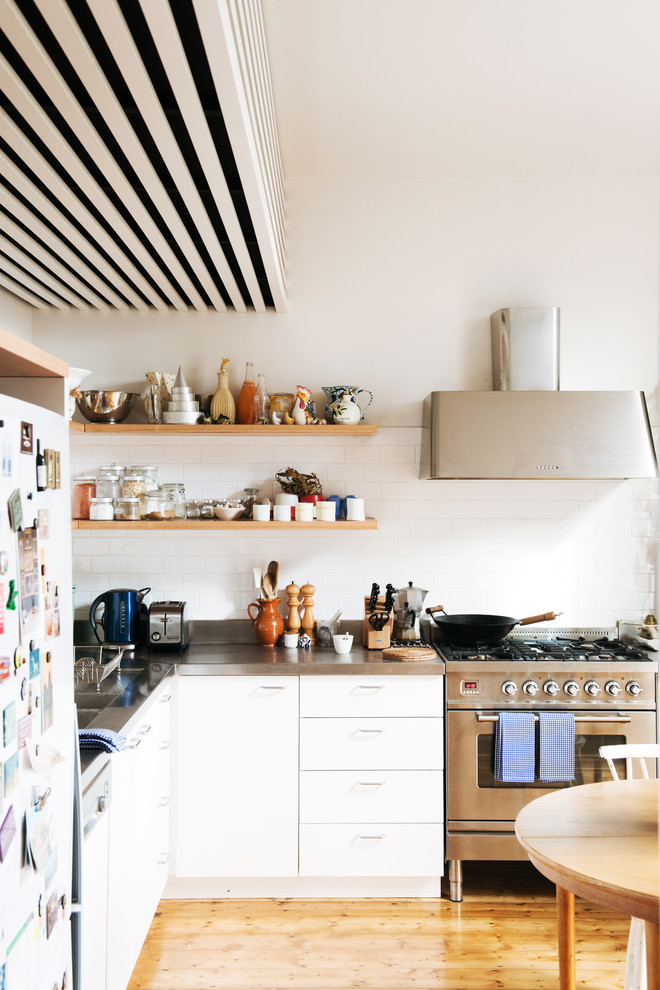 Idéer för mellanstora skandinaviska l-kök, med luckor med profilerade fronter, vita skåp, bänkskiva i rostfritt stål, vitt stänkskydd, stänkskydd i keramik, rostfria vitvaror och ljust trägolv