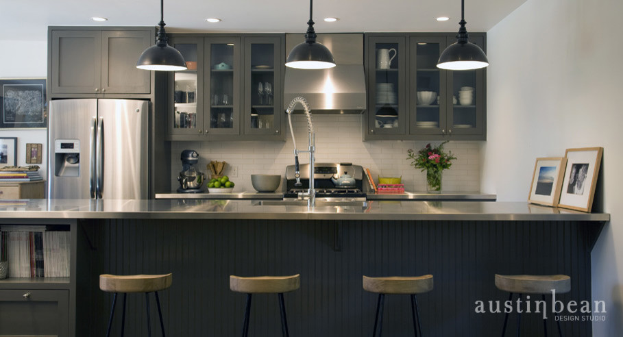 Klassisk inredning av ett kök, med en integrerad diskho, luckor med glaspanel, grå skåp, bänkskiva i rostfritt stål, vitt stänkskydd, stänkskydd i tunnelbanekakel och rostfria vitvaror