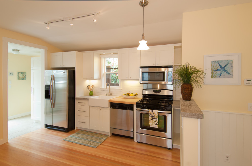 Immagine di una cucina lineare classica con elettrodomestici in acciaio inossidabile, lavello stile country e ante bianche
