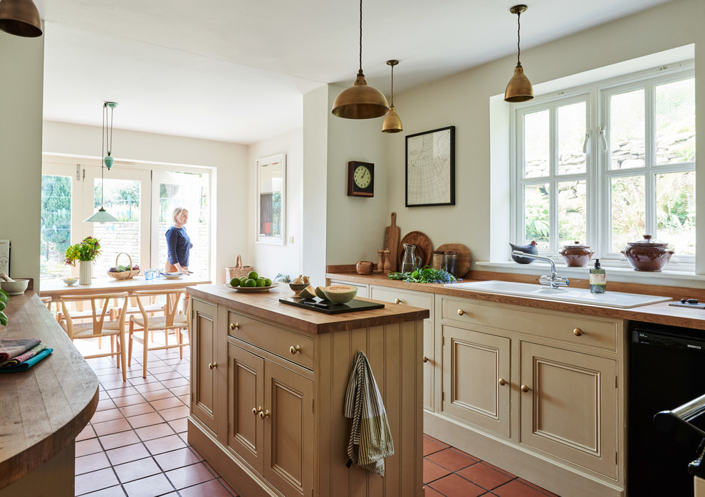Foto på ett mellanstort lantligt kök och matrum, med luckor med upphöjd panel, beige skåp, träbänkskiva, blått stänkskydd, stänkskydd i keramik, svarta vitvaror, klinkergolv i terrakotta och en köksö