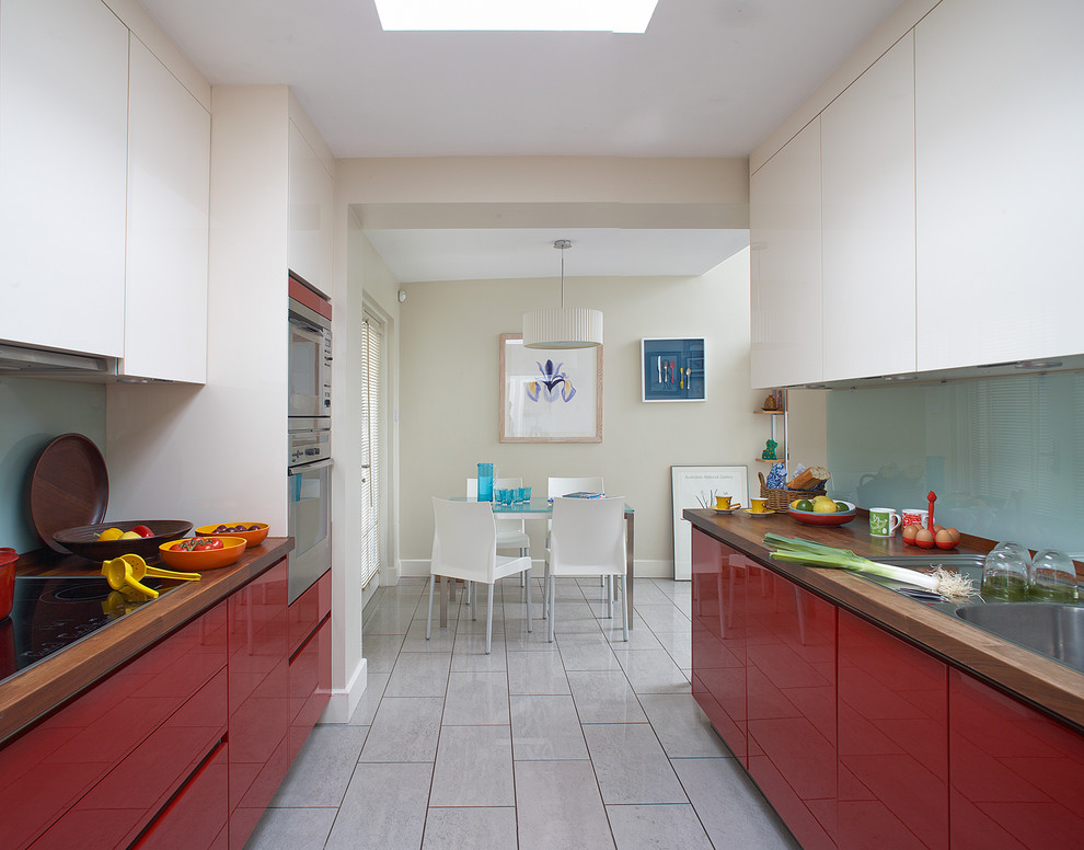 Réalisation d'une cuisine américaine parallèle design avec un plan de travail en bois, un évier posé, un placard à porte plane, des portes de placard rouges, une crédence bleue et une crédence en feuille de verre.
