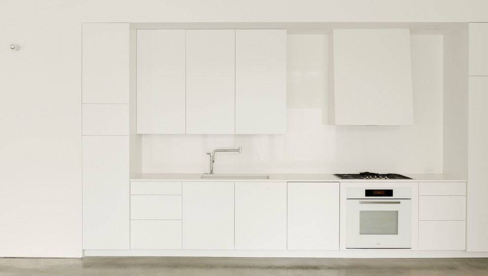 Immagine di una cucina design di medie dimensioni con lavello sottopiano, ante lisce, ante bianche, top in superficie solida, paraspruzzi bianco, elettrodomestici bianchi, pavimento in cemento e nessuna isola