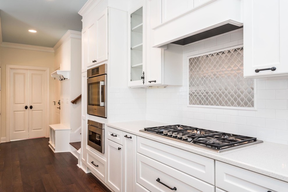 This is an example of a large classic l-shaped open plan kitchen in Raleigh with a belfast sink, shaker cabinets, white cabinets, granite worktops, white splashback, ceramic splashback, stainless steel appliances, medium hardwood flooring and an island.