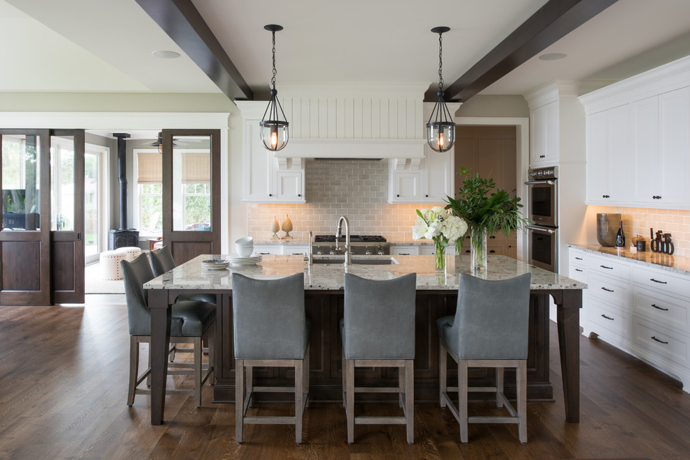 Photo of a large traditional l-shaped open plan kitchen in Minneapolis with recessed-panel cabinets, white cabinets, grey splashback, stainless steel appliances, dark hardwood flooring, an island, a double-bowl sink, granite worktops, ceramic splashback and brown floors.