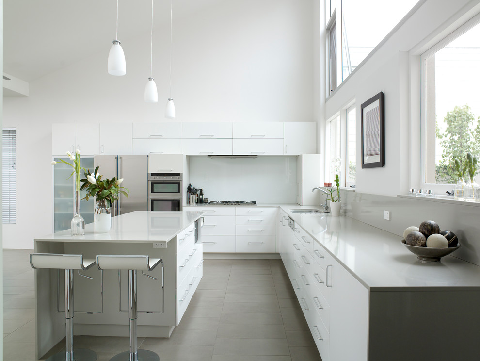 Idéer för ett modernt kök, med en köksö, en undermonterad diskho, släta luckor, vita skåp, vitt stänkskydd, rostfria vitvaror och grått golv