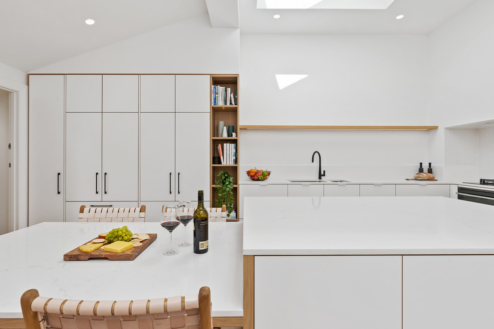 Foto på ett mellanstort minimalistiskt vit kök, med en undermonterad diskho, släta luckor, vita skåp, bänkskiva i kvarts, vitt stänkskydd, stänkskydd i mosaik, svarta vitvaror, mellanmörkt trägolv, en köksö och brunt golv