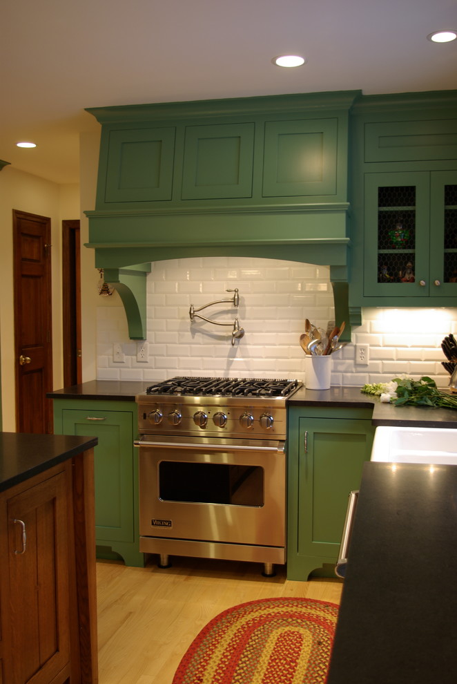 Inspiration for a medium sized classic u-shaped kitchen/diner in Milwaukee with a belfast sink, recessed-panel cabinets, green cabinets, granite worktops, white splashback, ceramic splashback, stainless steel appliances, light hardwood flooring and an island.