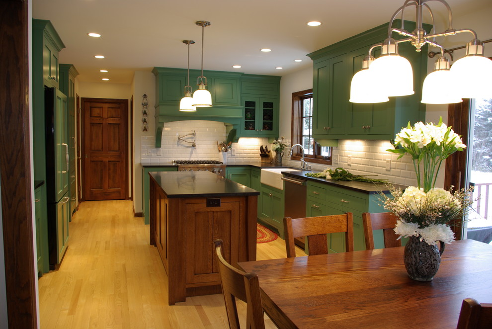 Design ideas for a medium sized classic u-shaped kitchen/diner in Milwaukee with a belfast sink, recessed-panel cabinets, green cabinets, white splashback, ceramic splashback, stainless steel appliances, light hardwood flooring, an island and granite worktops.