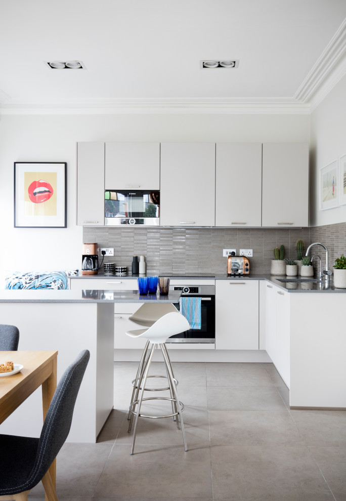 Foto på ett mellanstort funkis grå kök, med en undermonterad diskho, släta luckor, vita skåp, grått stänkskydd, rostfria vitvaror, klinkergolv i porslin, en köksö och grått golv