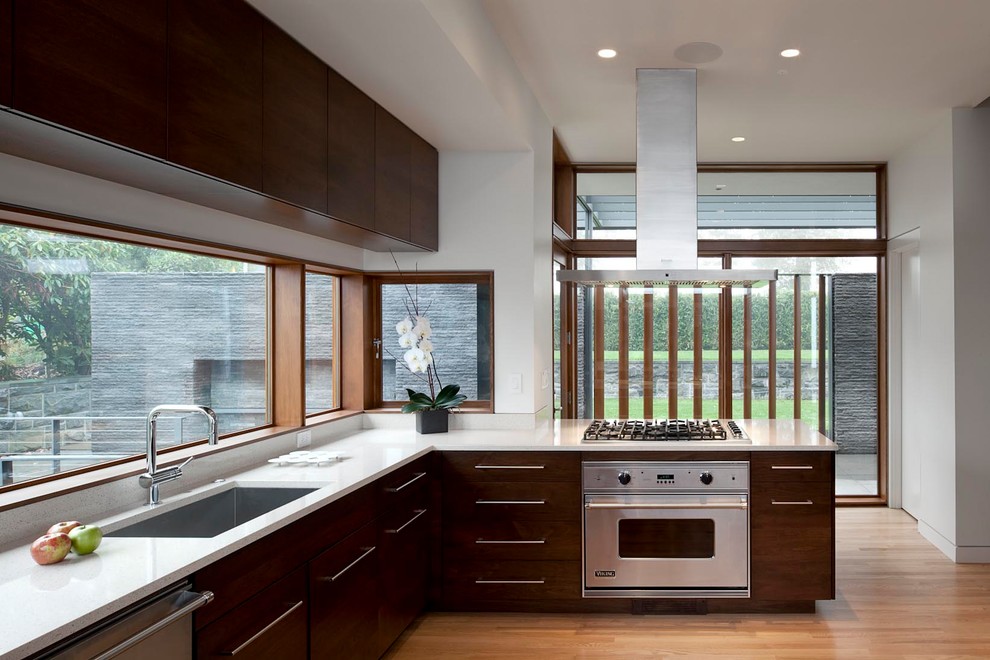 Inspiration for a medium sized contemporary l-shaped enclosed kitchen in Portland with a submerged sink, flat-panel cabinets, stainless steel appliances, medium hardwood flooring, a breakfast bar, dark wood cabinets, window splashback and brown floors.