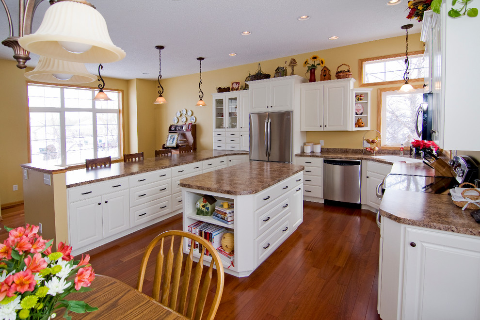 Exempel på ett mellanstort klassiskt kök, med en integrerad diskho, luckor med upphöjd panel, vita skåp, laminatbänkskiva, rostfria vitvaror, en köksö, mellanmörkt trägolv och brunt golv