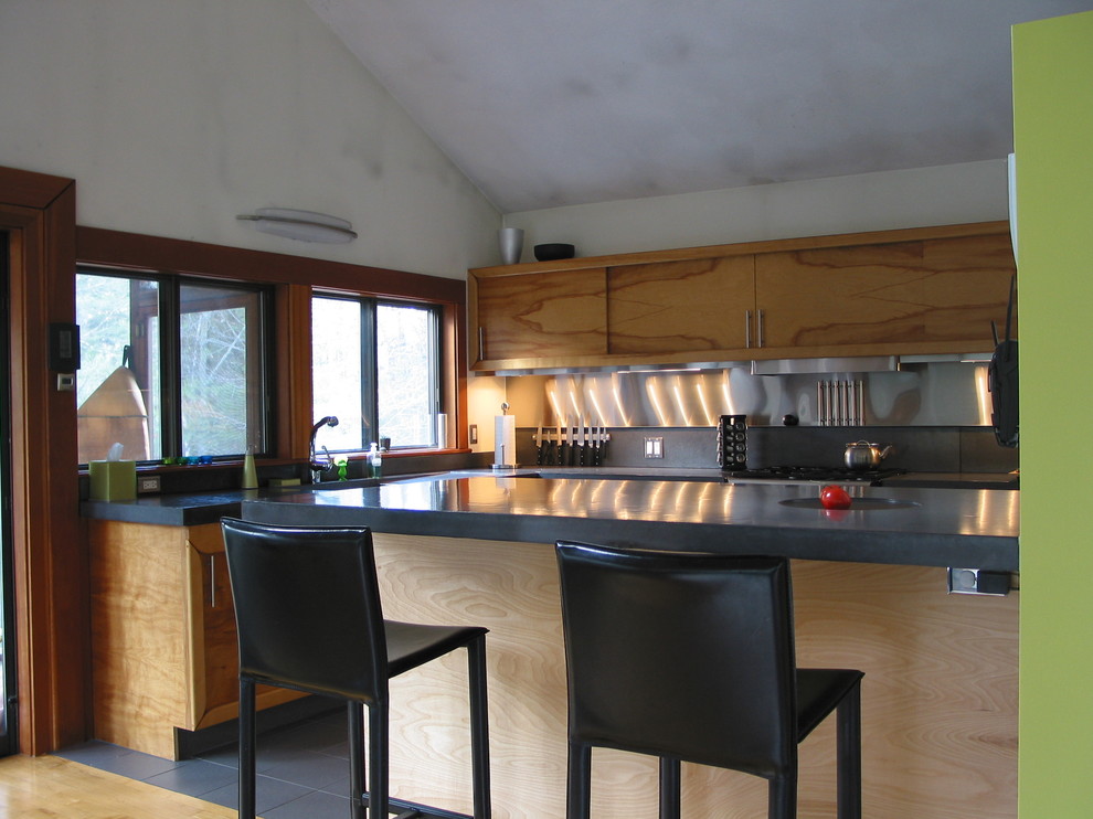 Modern inredning av ett l-kök, med skåp i mellenmörkt trä och stänkskydd med metallisk yta