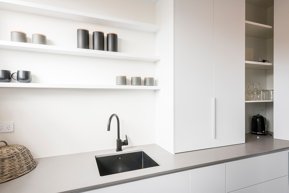 Inspiration for a small contemporary u-shaped kitchen pantry in Auckland with a built-in sink, raised-panel cabinets, white cabinets and grey worktops.