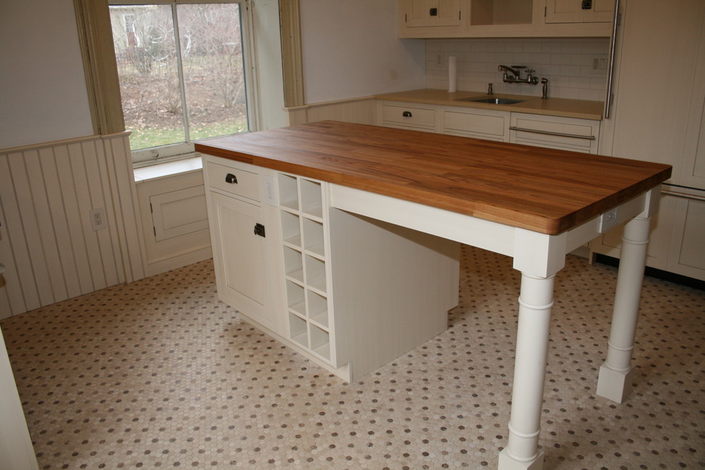 Bild på ett mellanstort lantligt linjärt kök och matrum, med en undermonterad diskho, luckor med infälld panel, vita skåp, träbänkskiva, vitt stänkskydd, stänkskydd i keramik, integrerade vitvaror och en köksö