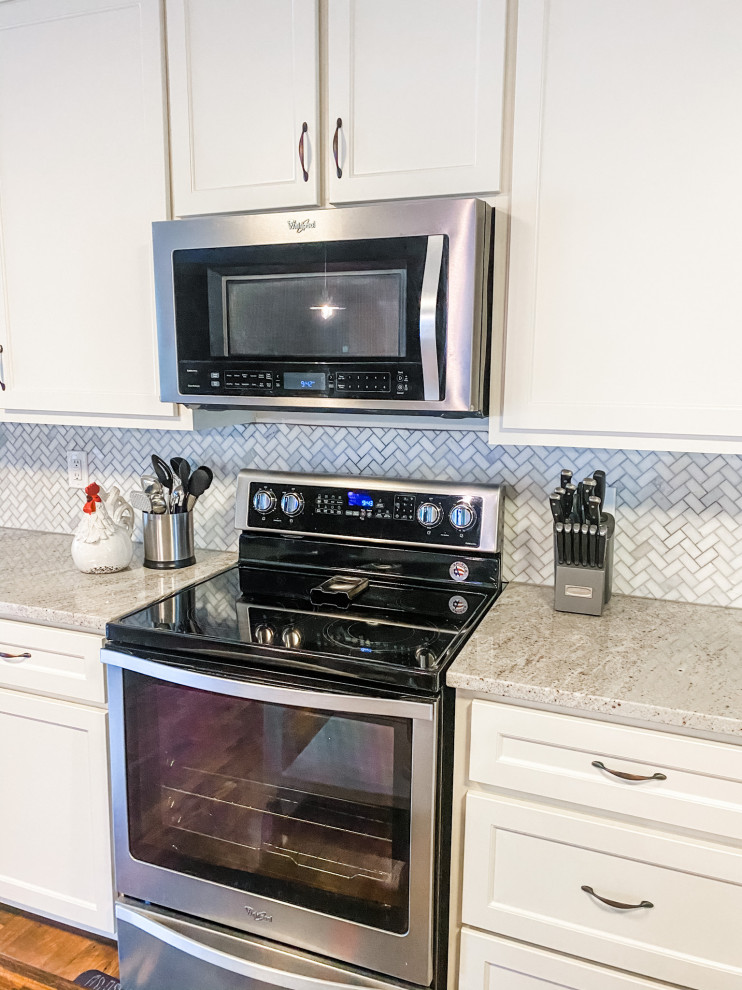 Foto på ett stort lantligt grå kök, med en undermonterad diskho, skåp i shakerstil, vita skåp, granitbänkskiva, grått stänkskydd, stänkskydd i marmor, rostfria vitvaror, laminatgolv, en köksö och brunt golv