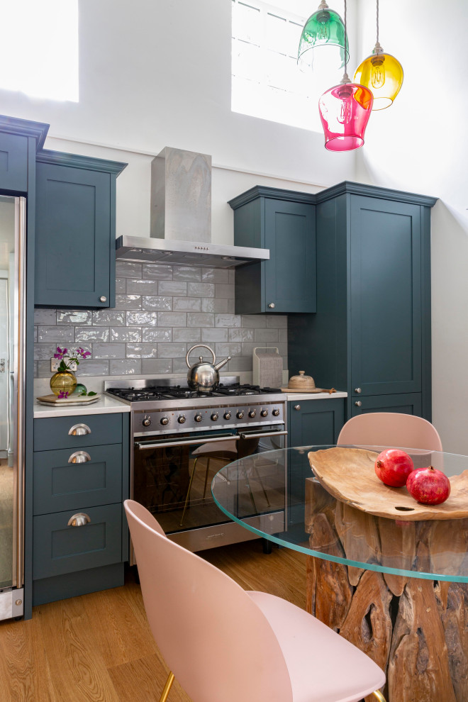 Foto på ett mellanstort vintage vit kök med öppen planlösning, med skåp i shakerstil, blå skåp, grått stänkskydd, stänkskydd i keramik, rostfria vitvaror och brunt golv