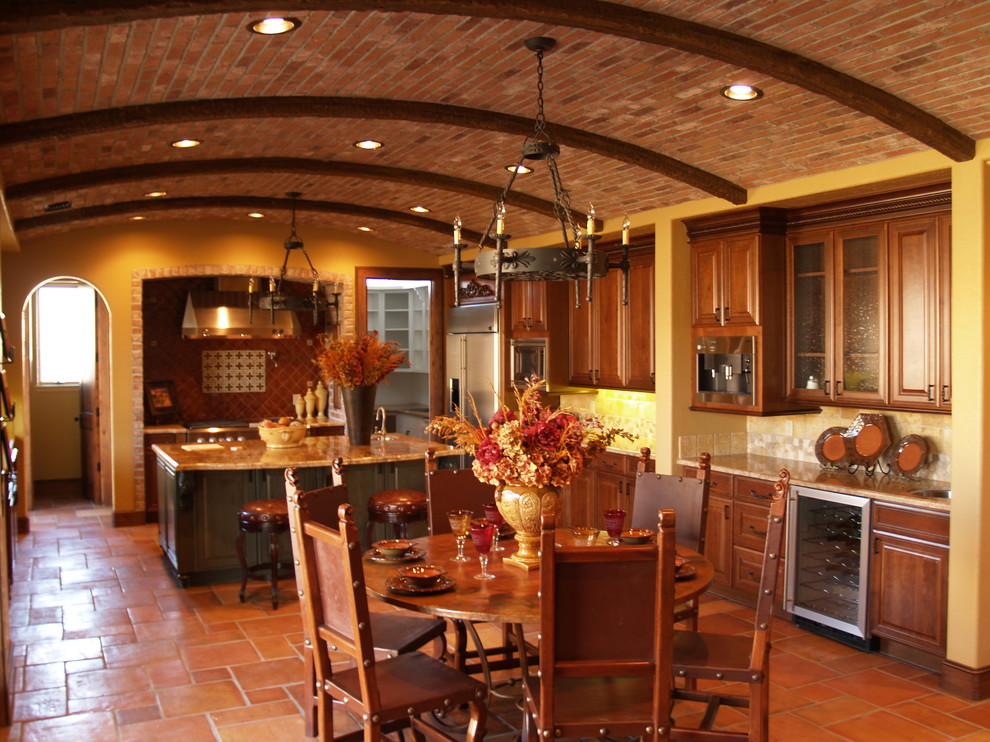 На фото: кухня в средиземноморском стиле с фасадами с выступающей филенкой, мраморной столешницей, обеденным столом, темными деревянными фасадами и полом из терракотовой плитки