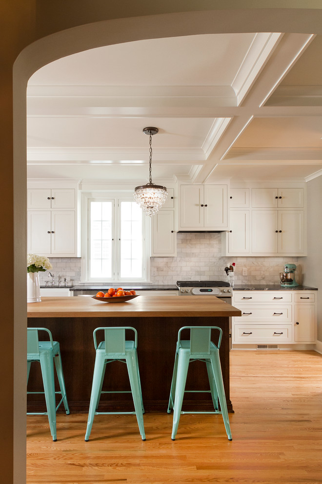 Inspiration for a large timeless single-wall light wood floor open concept kitchen remodel in Minneapolis with a farmhouse sink, shaker cabinets, white cabinets, wood countertops, gray backsplash, stone tile backsplash, stainless steel appliances and an island