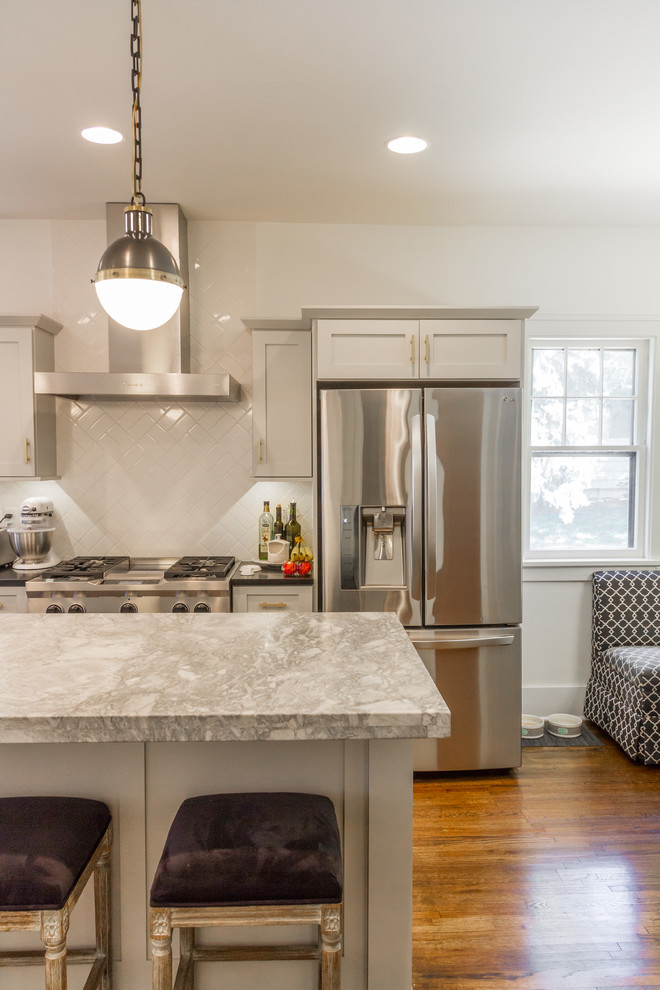 Mid-sized cottage l-shaped medium tone wood floor and brown floor enclosed kitchen photo in Other with white cabinets, marble countertops, white backsplash, subway tile backsplash, stainless steel appliances, an island, a farmhouse sink and recessed-panel cabinets