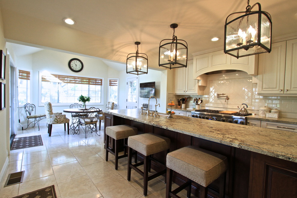 Exempel på ett avskilt, stort klassiskt u-kök, med en undermonterad diskho, luckor med upphöjd panel, vita skåp, granitbänkskiva, beige stänkskydd, stänkskydd i tunnelbanekakel, rostfria vitvaror, travertin golv och en köksö