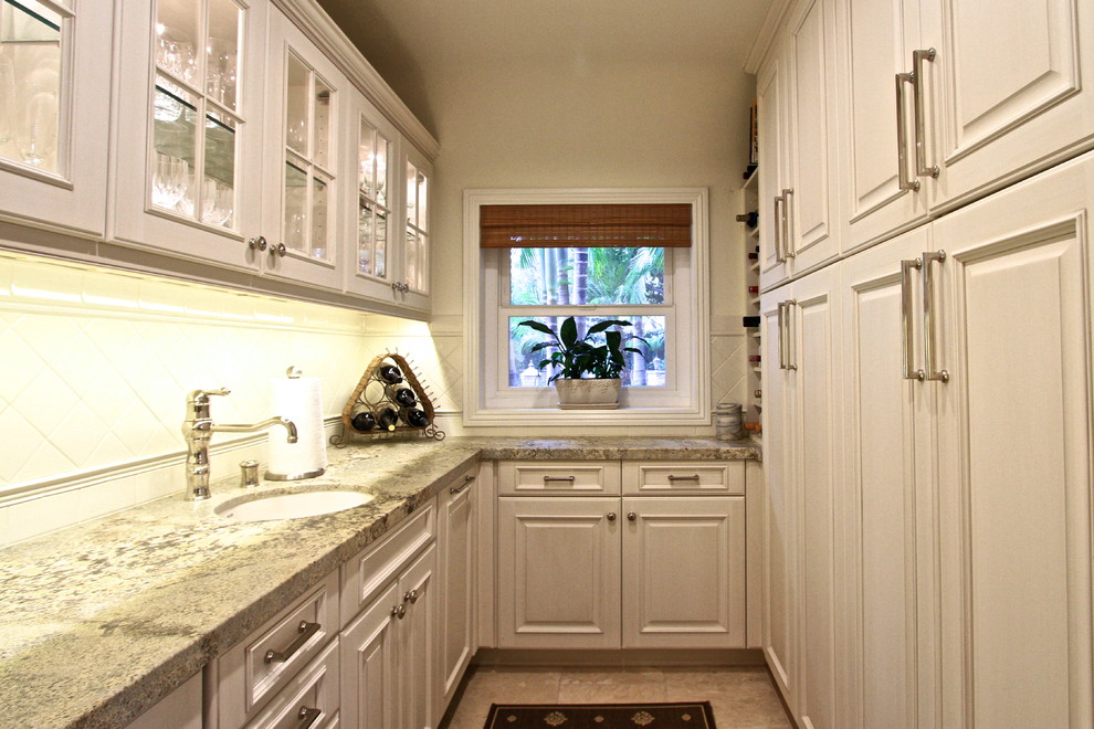 Klassisk inredning av ett avskilt, stort u-kök, med en undermonterad diskho, luckor med upphöjd panel, vita skåp, granitbänkskiva, vitt stänkskydd, stänkskydd i tunnelbanekakel, rostfria vitvaror, travertin golv och en köksö
